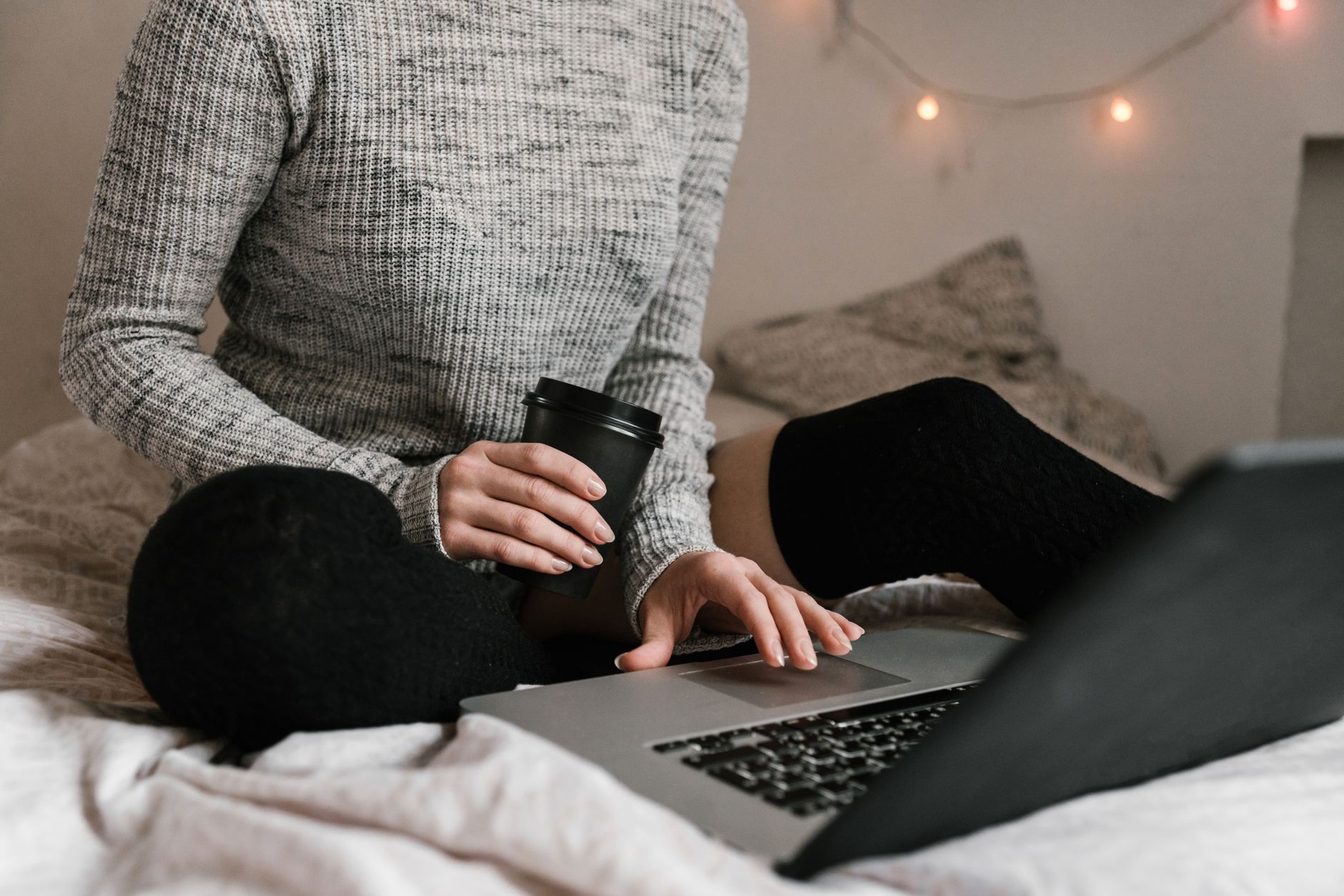 Iemand leest een boek naast een kop koffie en een laptop op een houten tafel